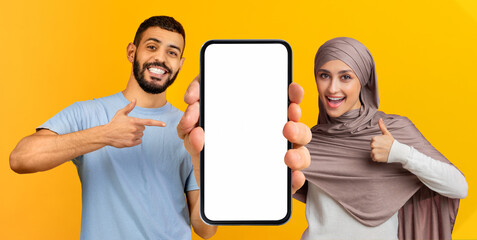 Cheerful Islamic Couple Pointing At Big Blank Smartphone And Showing Thumb Up