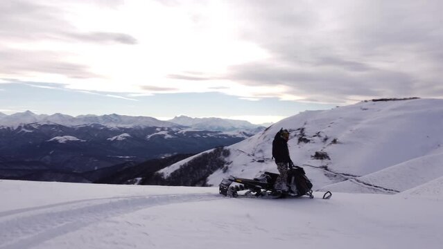 A man on a snowmobile roams the mountains 2023 filming from a drone