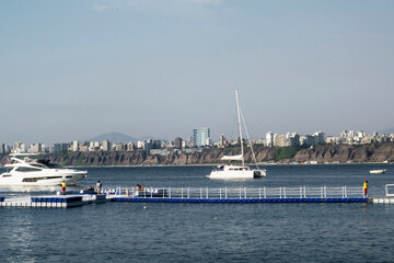 Chorillos Peru-June 2017-Plastic pier and luxurious yachts, people sunbathing in the Pacific ocean, modern buildings in the background