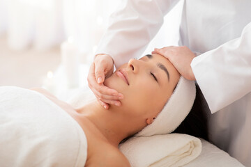 Fototapeta na wymiar Masseuse Lady Making Face Lifting Massage To Indian Woman In Spa Salon