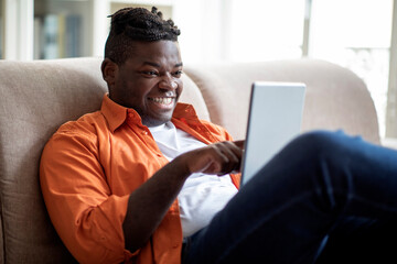 Happy cool chubby black guy using digital tablet at home