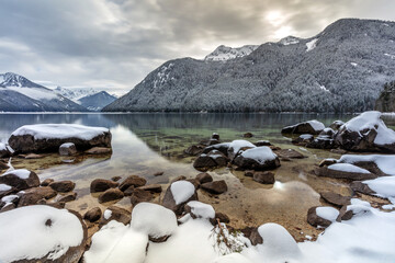 Snow on rocks at lake shore with reflection of mountains in winter