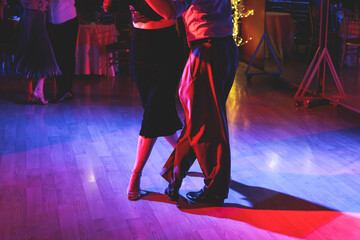 Fototapeta premium Couples dancing traditional latin argentinian dance milonga in the ballroom on a festival, tango studio, salsa, bachata and kizomba lesson in the red and purple lights, rehearsal in the dance class