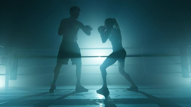 Close-up shot of a man training a woman at the gym. Unrecognized coach working out with female kickboxer indoors. High quality 4k footage in cold teal blue foggy back light
