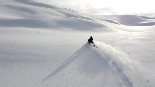 A man on a snowmobile roams the mountains 2023 filming from a drone