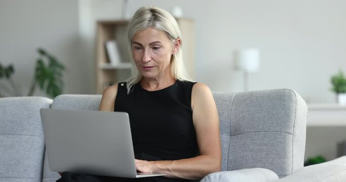 Smiling Mature Woman Sits On Couch With Laptop. Attractive Middle-aged 50s Female Relax At Home, Spend Pleasant Leisure On Internet, Working, Web Surfing On-line, Enjoy Social Media, Modern Tech Usage