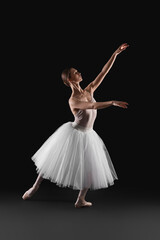 Young ballerina practicing dance moves on black background