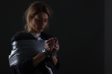 Scared woman taped up and taken hostage on dark background. Space for text