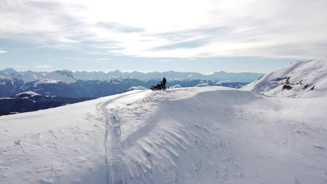 A man on a snowmobile roams the mountains 2023 filming from a drone