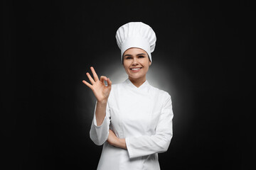 Happy female chef with wooden spoon showing ok gesture on black background