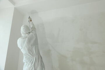 Decorator painting wall with spray, back view. Space for text