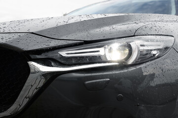 Car with switched on headlight in drops of water, closeup