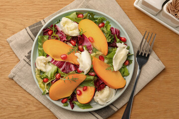 Delicious persimmon salad with cheese and pomegranate served on wooden table, flat lay