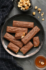 Plate with delicious chocolate bars, caramel and nuts on black table, flat lay