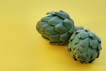 Obraz premium Whole fresh raw artichokes on yellow background, closeup. Space for text