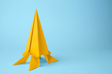 Origami art. Handmade yellow paper rocket on light blue background, space for text