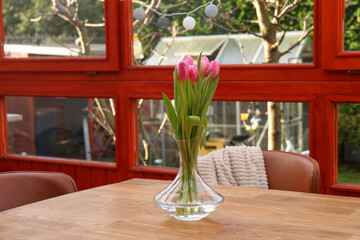 Pink tulips in glass vase on wooden table at terrace