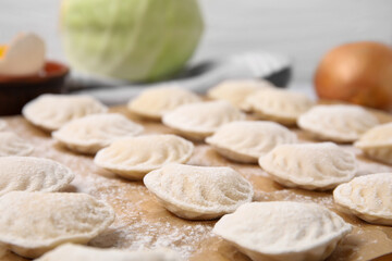 Fototapeta na wymiar Raw dumplings (varenyky) with tasty filling and flour on parchment paper, closeup view