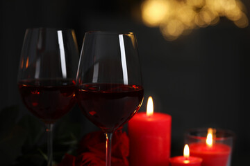 Glasses of red wine, burning candles and rose flowers against blurred lights, space for text. Romantic atmosphere