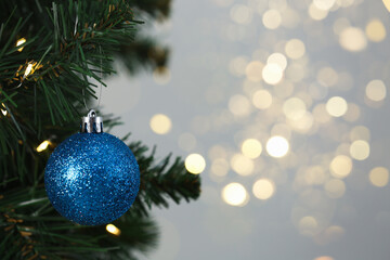Blue shiny ball hanging on Christmas tree against grey background. Space for text