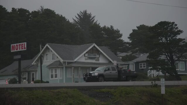 Side view of a passenger car driving along the road with a motel building on side. Traditional American architecture with cloudy skyline above. High quality 4k footage