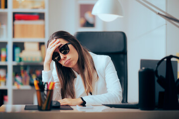 Tired Office Worker Wearing Sunglasses at the Office. Woman suffering from photosensitivity to...