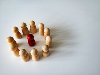 Red wooden doll figure surrounded by other doll figure on white background. Harassment and bully...