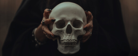 skull of a dead man in the hands of a witch witch in a black costume for an occult satanic ritual....