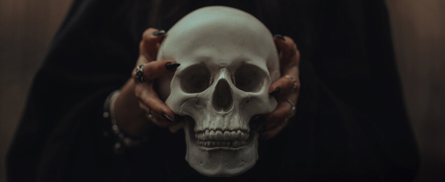 skull of a dead man in the hands of a witch witch in a black costume for an occult satanic ritual. Panoramic wide horizontal photo for banner head cover