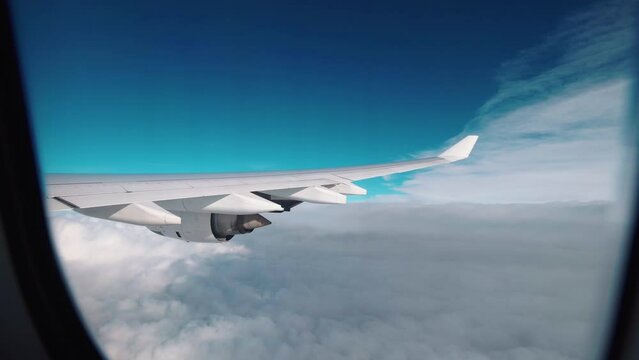 Airplane flight. Wing of an airplane flying above the clouds. Looking through window aircraft during flight in wing. Side view from a plane window of the aircraft wing and clouds. Travel and holidays 