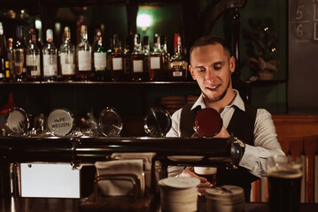 bartender pours draft beer into a glass from tap behind the bar counter in pub