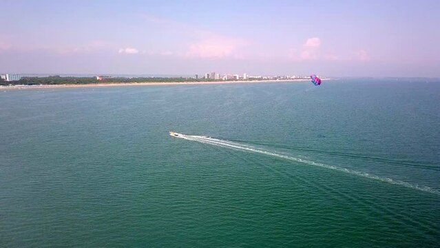 aerial drone shot of boat pulling parachute over the sea in lignano parasailing