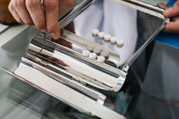 Closeup image hand of pharmacist counting and arrange pills on qualified stainless counting tray with spatula in pharmacy. Pharmacist prepare medication in stainless tray by prescription at drugstore.