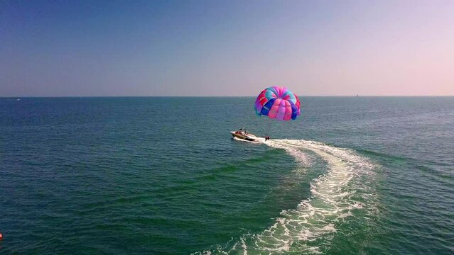 aerial drone shot of boat pulling parachute over the sea in lignano parasailing