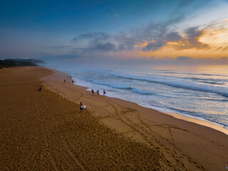 Hazy Summer sunrise at the seaside with surfers and photographers