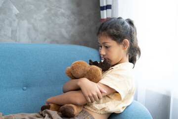 Cute little casual girl embracing teddy bear. Sad kid playing at home, sitting on sofa with teddy bear sitting on sofa at home , copy space