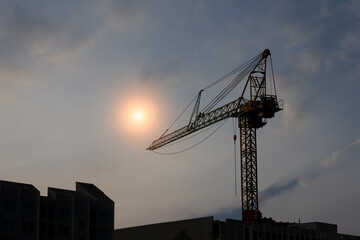 The silhouette of a tower crane sits on top of the building in the dark clouds that obscure the sun.