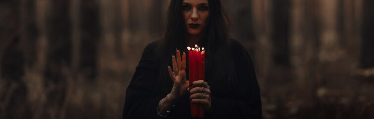 dark terrible witch with candles in her hands performs an occult mystical ritual in the forest....