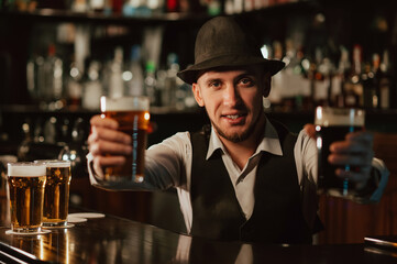 happy bearded bartender at bar counter with glasses of beer in pub