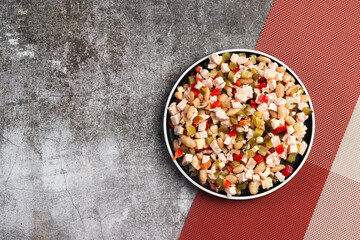 Smoked chicken salad with pickled cucumbers, white beans, bell peppers on a round plate on a dark background. Top view, flat lay
