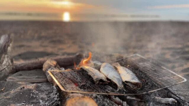 Grilling fish on simple sandy beach barbecue with blurred sunset horizon