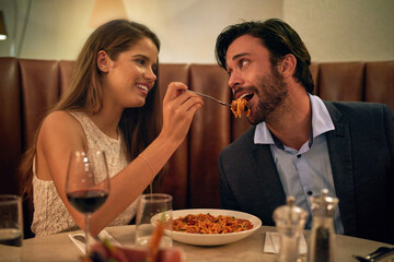 Love, restaurant date and woman feeding man spaghetti on valentines day, happy and romantic dinner. Romance, valentine and food with wine, couple celebrate marriage or relationship with time together