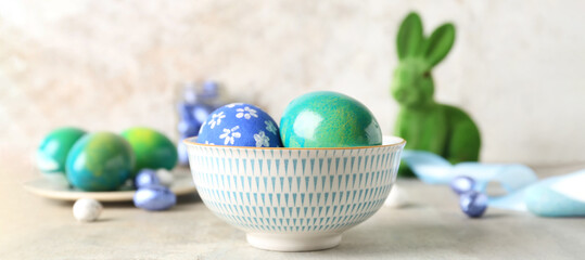 Bowl with painted Easter eggs on light background