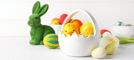 Basket with painted Easter eggs and bunny on light background