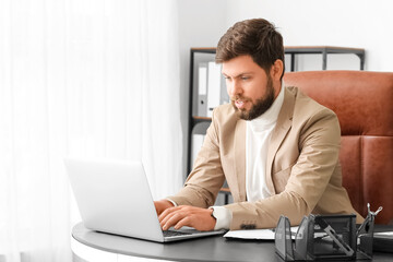 Handsome young businessman working with laptop at table in office