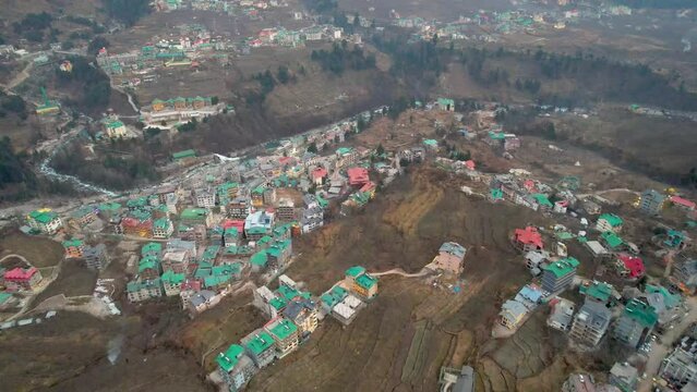 aerial drone shot flying forward over colorful houses, busy kullu manali highway beas river and hamta village on himalaya mountain in distance