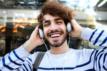 Happy young man relaxing outdoors listening to music using headphones looking at camera.