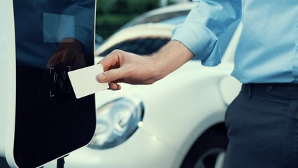A man use his credit card to pay for eco-friendly clean and sustainable energy for his electric vehicle at charging station. Progressive man pay for charging point to power his rechargeable vehicle.