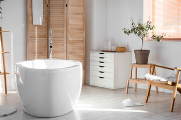 Interior of light bathroom with drawers, bathtub and folding screen