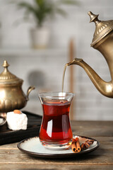 Pouring of hot Turkish tea from teapot into glass on wooden table, closeup